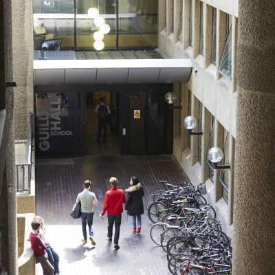 Students walk into Guildhall Silk Street building entrance on a sunny day